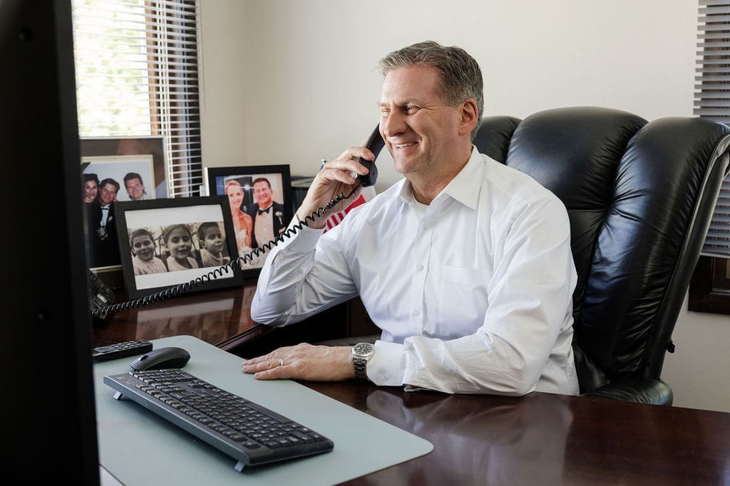 Alt Text Alt Text: Peter Wachowski, Chicago personal injury attorney, smiling while speaking on the phone with a client at his office desk.