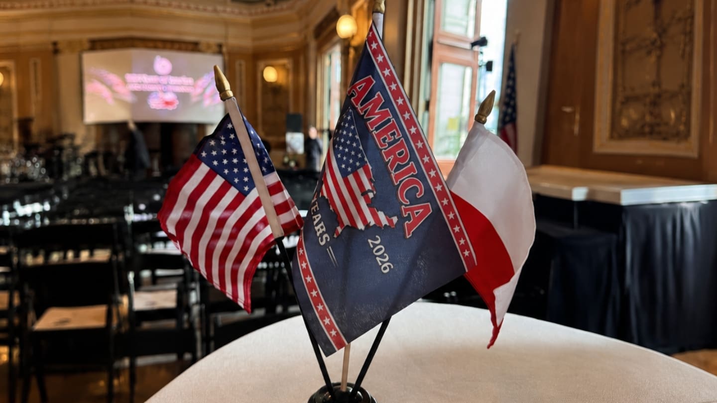 American, Polish, and commemorative "America 250 Years" flags displayed on a table at the Polish American Congress event in Washington, D.C.
